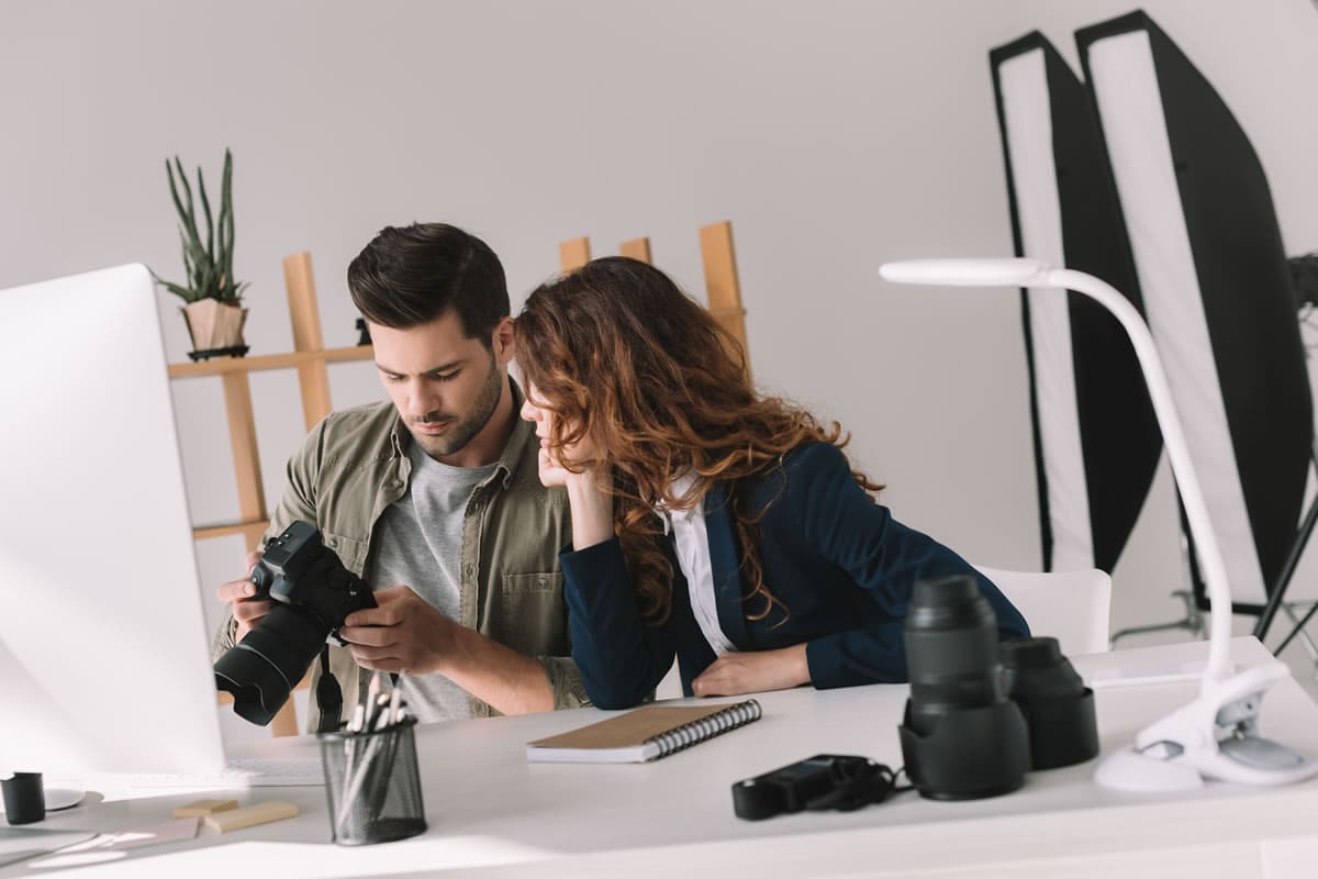 Un hombre y una mujer mirando una cámara en un estudio de fotografía. SEO para Fotógrafos