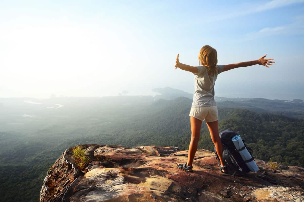 Una mujer está parada en la cima de una montaña con los brazos extendidos, experimentando la impresionante belleza de la naturaleza. Este impresionante paisaje es un ejemplo perfecto del inmenso potencial para el turismo.