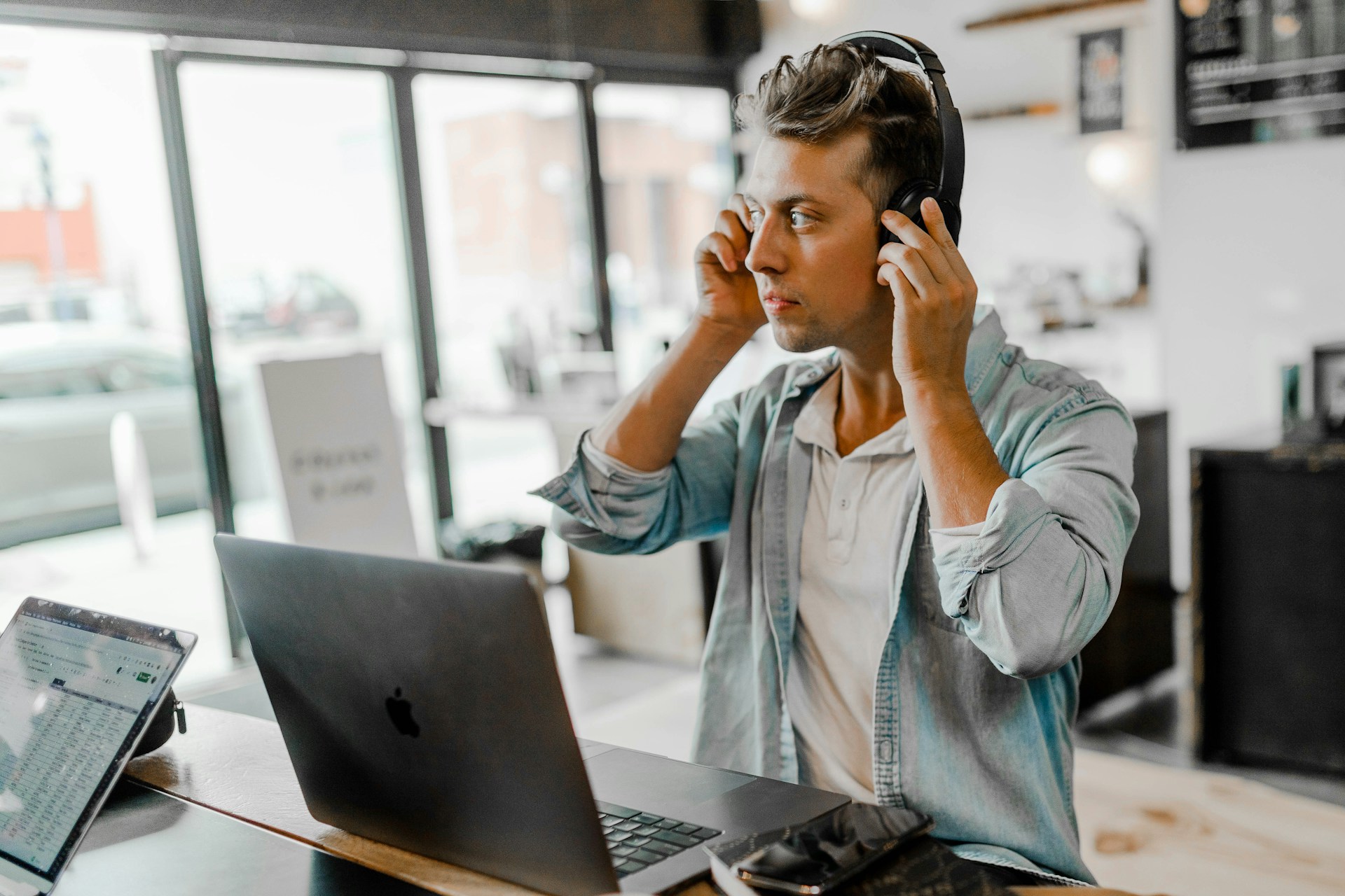 Una persona sentada en una mesa con un portátil, con auriculares y mirando fijamente la pantalla en una habitación bien iluminada y con grandes ventanales, claramente centrada en analizar los resultados SEO.