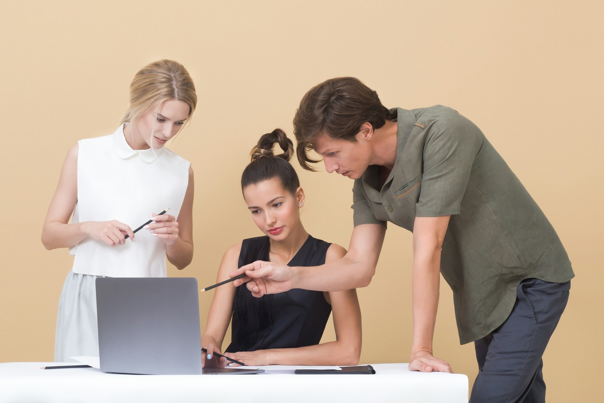 Tres personas colaboran en una mesa con un portátil. Una persona está sentada mientras las otras dos están de pie, apuntando a la pantalla del portátil, discutiendo reseñas de Google para su próximo gran proyecto.