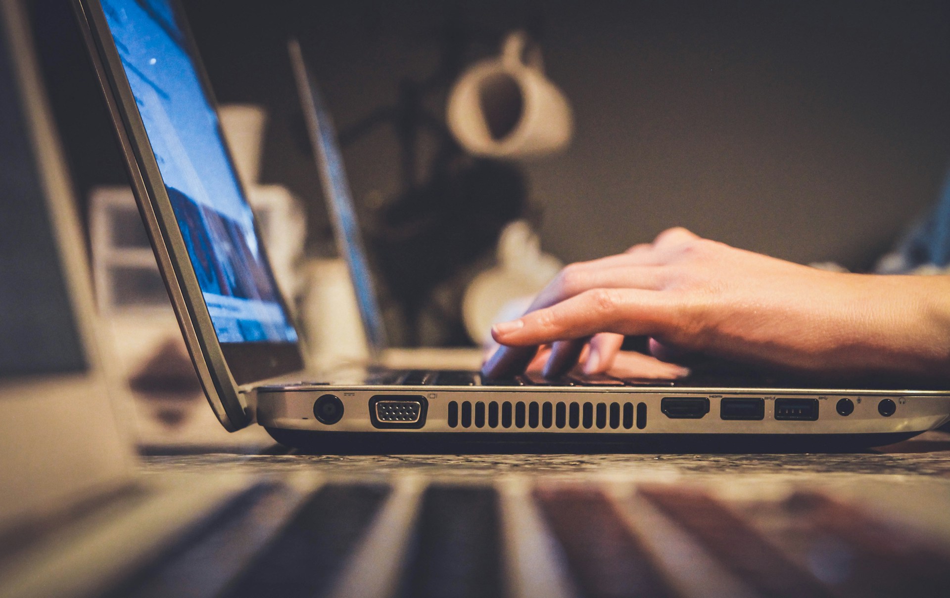 Una persona está escribiendo en una computadora portátil, con otros dispositivos electrónicos visibles a los lados, posiblemente verificando si hay contenido duplicado.