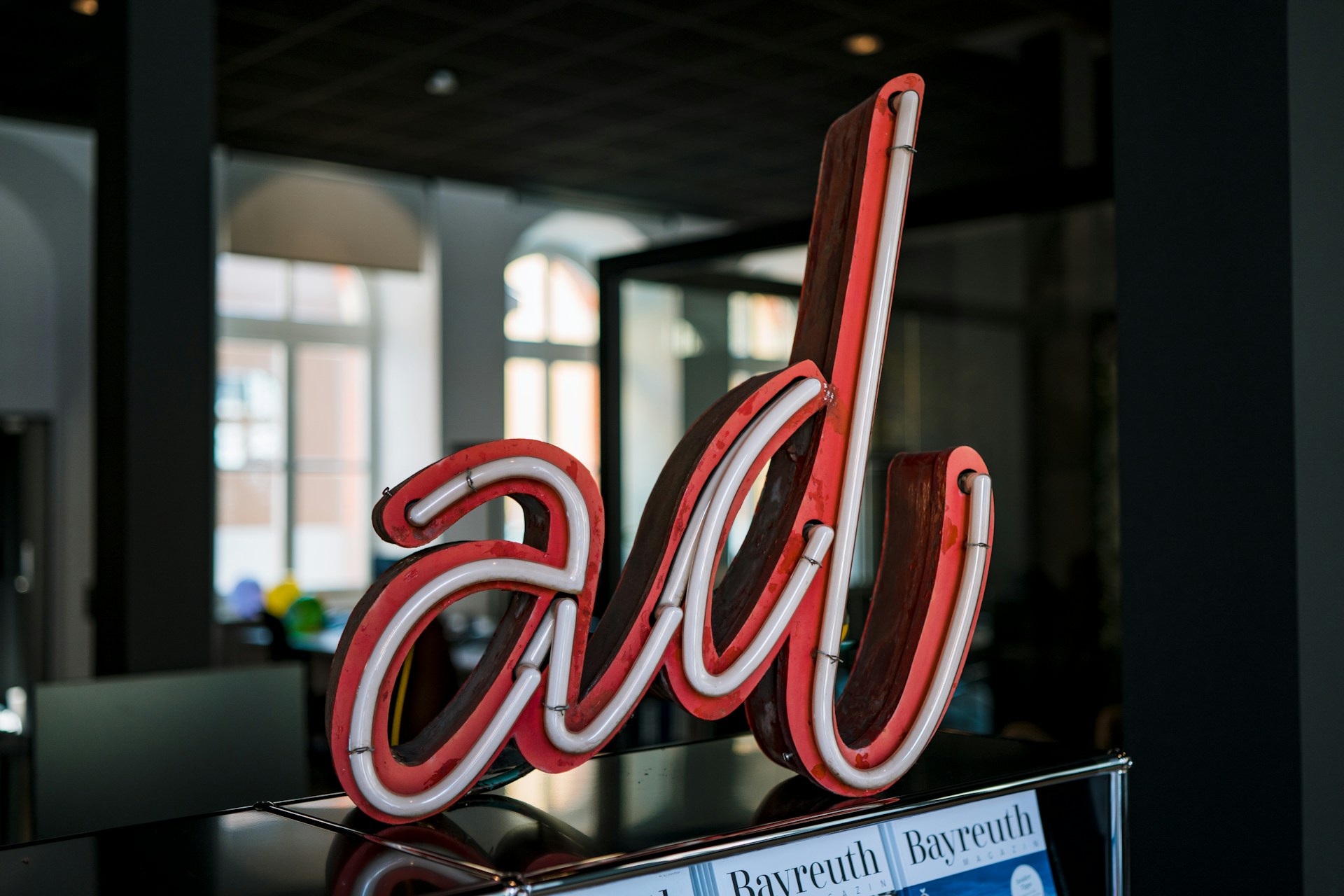 En el interior se exhibe un letrero de neón con la forma de las letras "alb", con un interior oscuro y ventanas arqueadas al fondo, creando una atmósfera perfecta para discutir estrategias de Publicidad en Buscadores.