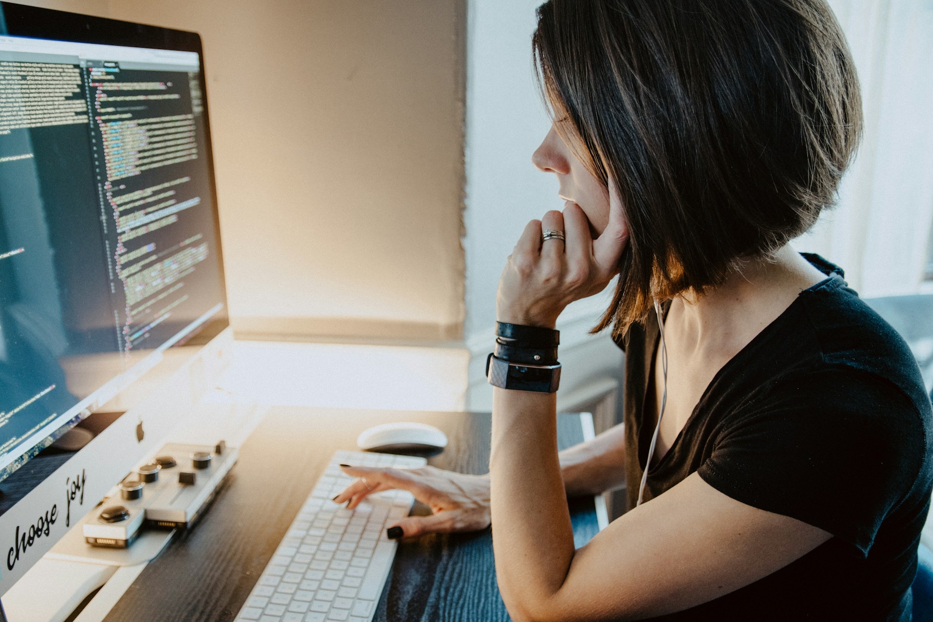 Una persona con cabello corto se sienta en un escritorio, escribe en un teclado y mira la pantalla de una computadora que muestra un código. Su enfoque es nítido mientras depuran los enlaces rotos para garantizar una funcionalidad fluida.