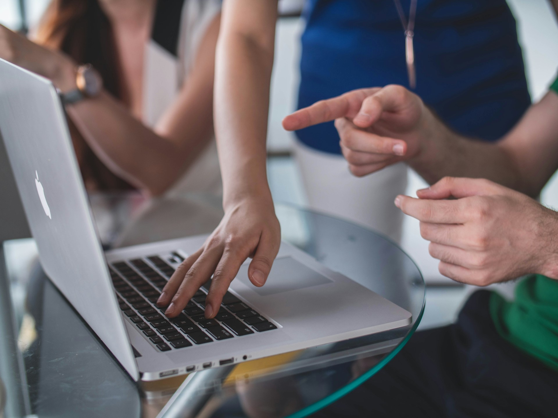 Tres personas están reunidas alrededor de una computadora portátil. Una persona toca el teclado, mientras otras dos señalan la pantalla, posiblemente discutiendo su estrategia de redacción SEO.