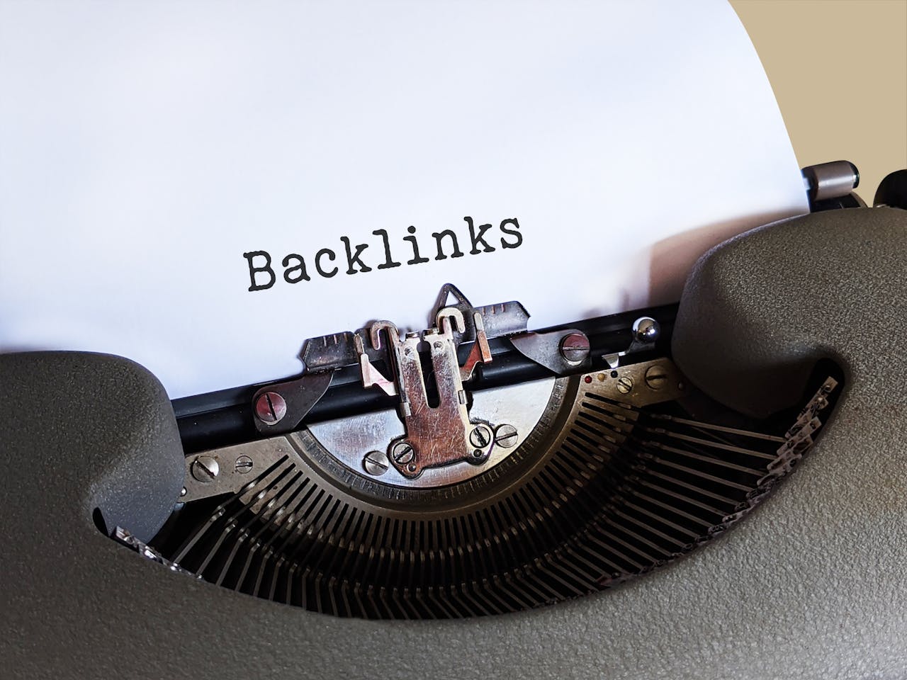 Un primer plano de una máquina de escribir antigua con una hoja de papel blanca que muestra la palabra "Backlinks" escrita, enfatizando la importancia de los backlinks para posicionarme en Google.