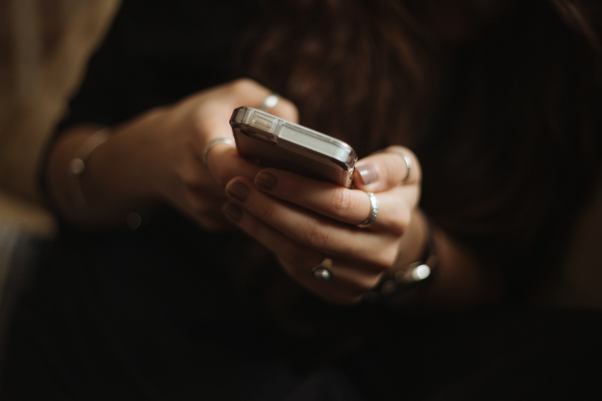 Una persona que sostiene un teléfono inteligente con ambas manos enfoca atentamente el dispositivo. Múltiples anillos y pulseras adornan sus dedos y muñecas, añadiendo un toque de estilo personal. Con este enfoque, pretenden mejorar los anuncios en línea para lograr una mejor participación.