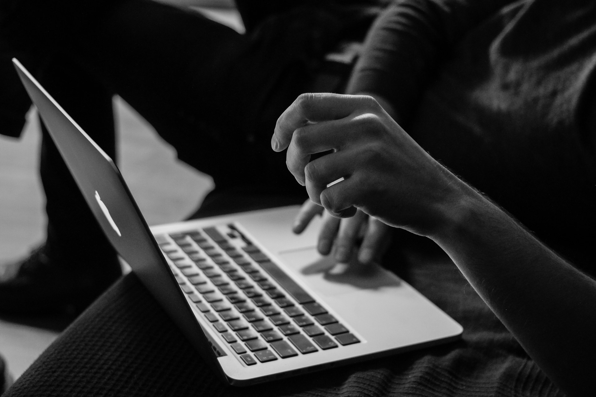 Persona que utiliza una computadora portátil abierta con ambas manos, una sobre el teclado y la otra ligeramente elevada por encima de él, como si considerara el volumen de búsqueda de Palabras Clave. La imagen está en blanco y negro.