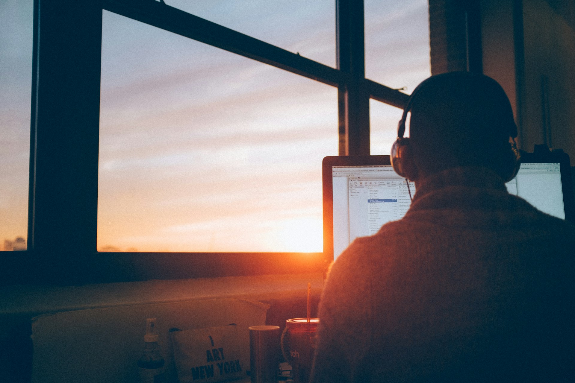 Persona que usa audífonos trabajando en una computadora cerca de una ventana durante el atardecer, optimizando meta descripciones y títulos para mejorar el CTR.