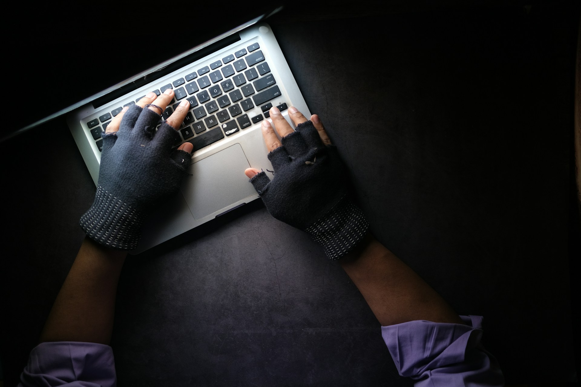 Una persona que usa guantes negros sin dedos está escribiendo en el teclado de una computadora portátil, tal vez usando Copyscape para asegurarse de que su contenido sea original y evitar el plagio en su sitio web.