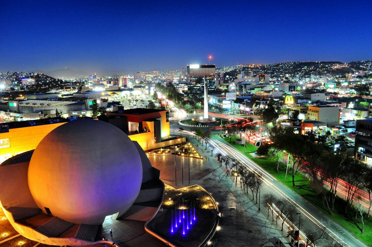 Vista aérea de Tijuana de noche, donde se puede apreciar el edificio esférico del Centro Cultural de Tijuana. Las luces de la ciudad iluminan las calles y los edificios, con un horizonte vibrante al fondo: una ciudad conocida no solo por sus vistas, sino también por su próspera ciudad.